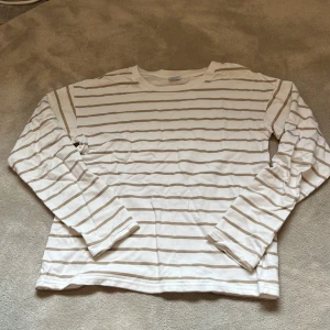 Vit och beige randig långärmad tröja från Lindex - Säljer en vit långärmad tröja med beigea ränder från Lindex. Tröjan har klassisk passform och är tillverkad i mjukt bomullsmaterial. Perfekt för en avslappnad stil. Hör av er vid frågor eller intresse❤️