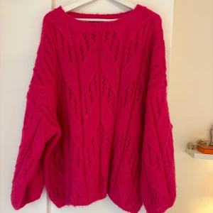 Rosa stickad tröja från Vero Moda - Säljer en ceriserosa stickad tröja från Vero Moda med oversize-passform. Tröjan har ett snyggt hålmönster och långa ärmar. Perfekt för att liva upp garderoben med en färgklick!