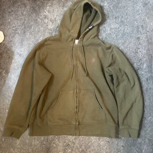 Hoodie The North Face L - Säljer en olivgrön hoodie från The North Face med dragkedja och huva. Tröjan har två stora fickor framtill och justerbara snören i huvan. 