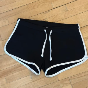 Svarta mjukisshorts med vit kant - Svarta mjukisshorts från med vit kant och snörning i midjan. Storlek M. Oanvända.
