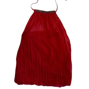 Röd halterneck topp med strassdetalj - Säljer en röd halterneck topp Bella Hadid inspirerad med plisserat tyg och strassdetaljer vid halsen. Toppen är ärmlös och har en luftig passform, perfekt för att sticka ut. Snygg till både jeans och kjol!