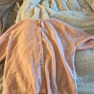 Ljusrosa kofta från 157 - Säljer en söt ljusrosa kofta från 157 i storlek S. Koftan har långa ärmar och knäpps med pärlknappar framtill. Mjuk och skön, perfekt för lager-på-lager. Passar dig som gillar en klassisk och enkel stil.