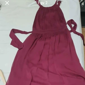 Vinröd långklänning med knytband - Säljer en vinröd långklänning med smala axelband som korsas i ryggen och knytband i midjan. Klänningen har en luftig och flowy passform, perfekt för sommarens tillfällen. Materialet känns lätt och bekvämt.