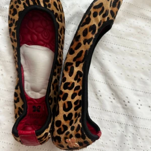 Leopardmönstrade ballerinaskor med röd innersula - Säljer ett par ballerinaskor från Butterfly Twists med leopardmönster och röd quiltad innersula. Skorna har svarta kanter och en liten guldfärgad detalj bak. Perfekta för dig som vill sticka ut med din stil!