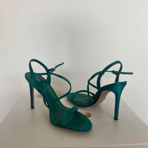 Smaragfärgsde sandaler med klack från Zara - Säljer ett par stilrena smaragds sandaler från Zara med smala remmar och hög klack. Skorna har öppen tå och en elegant design som passar perfekt till vår och sommar. Remmarna går runt vristen för extra stöd.