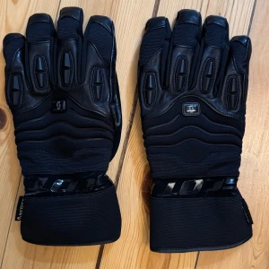 Svarta sportiga skinnhandskar från Scott - Svarta handskar från Scott med robust design och förstärkta partier på ovansidan. Gjorda i skinn med detaljer i syntetmaterial och breda muddar. Perfekta för dig som vill ha extra skydd och stilren look.