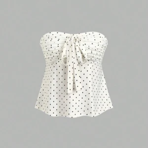 Vit prickig tubtopp med rosett - Säljer en söt vit tubtopp med svarta prickar och en dekorativ rosett framtill. Toppen är axelbandslös och har en lätt utsvängd passform. Perfekt för varma dagar eller somrig stil!