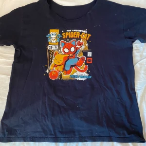 Svart t-shirt med Spider-Cat tryck - Cool svart t-shirt med färgglatt Spider-Cat tryck framtill. Motivet har en tecknad katt i Spider-Man-dräkt och texten 'The Amazing Spider-Cat'. Rund halsringning och korta ärmar. Perfekt för soctröja!