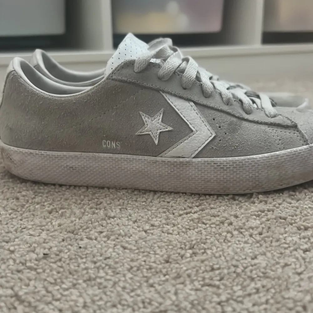 Säljer ett par stilrena grå sneakers från Converse med vit sula och snörning. Skorna har en klassisk stjärndetalj på sidan och är tillverkade i mocka för en snygg look. Perfekta för en avslappnad stil.. Kengät.