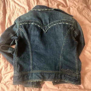 Mörkblå jeansjacka från Nolita - Snygg mörkblå jeansjacka från Nolita med dragkedja och knappar. Jackan har två bröstfickor med lock och knappar samt två snedställda fickor med dragkedja. Perfekt för en cool och avslappnad stil. Den är i st xl men passar s/m. Köparen står för frakten. 