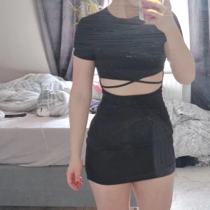 Svart kortklänning öppen. -  svart kortklänning med snörningsdetaljer i midjan. Klänningen har en tight passform och korta ärmar. Andvänd vid ett tillfälle.