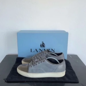 Grå sneakers från Lanvin - Snygga grå sneakers från Lanvin med en stilren design. Skorna har en rund tå och snörning framtill. Tillverkade i mocka med en kontrasterande beige sula och glansig tåhätta.