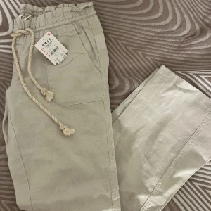 Beige linne byxor från Roxy - Säljer ett par linnebeige byxor från Roxy med elastisk midja och snörning. Byxorna har raka ben och praktiska fickor både fram och bak. Perfekta för en avslappnad stil. Helt nya säljs pga fel storlek 