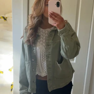 Grön jeansjacka - Säljer en snygg blå jeansjacka med knappar framtill. Jackan har en normal passform och långa ärmar. Perfekt för vår och höst! Säljer den här i blå!! INTE DEN PÅ BILDEN, SÄLJER EN BLÅ