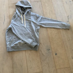 Grå hoodie från Polo Ralph Lauren - Säljer en HELT NYklassisk grå hoodie från Polo Ralph Lauren med vit dragsko och broderad logga på bröstet. Tröjan har känguruficka och mjukt material, perfekt för en avslappnad stil. Kostar 2000 från care of carl men mitt pris är 1699!!✅✅