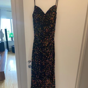 Festklänning/balkkänning  - Säljer en svart långklänning med tunna axelband och v-ringad urringning. Klänningen är täckt av färgglada paljetter och har snygg snörning i ryggen. Perfekt för fest eller bal när du vill sticka ut och glittra hela kvällen. OBS! Liten i storleken. I hemsidan stod det att man helst skulle gå upp en storlek. Jag som är normalt strl 38 var tvungen att gå upp till strl 40.  Köpt från Zalando nypris :3200kr Har en liten defekt som man ser på sista bilden!!!  Pris går att diskutera vid snabbaffär. 