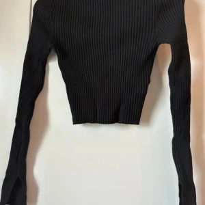 Svart ribbad croppad tröja från H&M - Säljer en svart ribbad croppad tröja från H&M. Tröjan har lång ärm och är figurnära med stretchigt material. Perfekt att styla med höga jeans eller kjol. Enkel och stilren design som passar till många tillfällen.