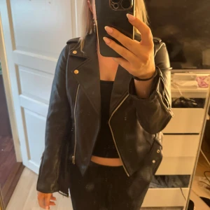 Svart skinnjacka från Glamorous - Säljer en svart skinnjacka från Glamorous köpt på Nelly.com. Jackan har silvriga dragkedjor, knappar och bälte i midjan. Snygg passform men säljer pga den inte kommer till användning💖💖 skriv vid frågor!