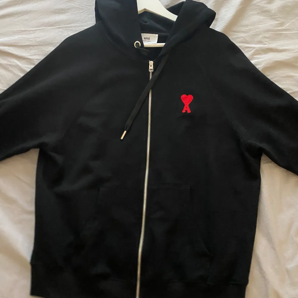 Svart hoodie från Ami med dragkedja och röd logga. mycket bra skick på tröjan. pris kan diskuteras vid snabb affär . Hupparit & Collegepaidat.