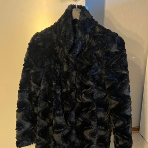 Svart pälsjacka från Vero Moda - Säljer en svart, fluffig päls kappa från Vero Moda. Den har lång ärm och en mjuk, vågig struktur i materialet. Perfekt för dig som vill ha en trendig  kappa med lite extra attityd.