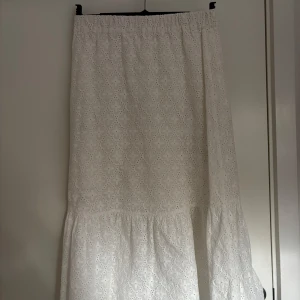 Vit långkjol med broderade detaljer - Säljer en vit långkjol med fina broderade mönster och volang nertill. Kjolen har resår i midjan och är perfekt för sommarens alla tillfällen. Lätt och luftig modell som ger en romantisk känsla.