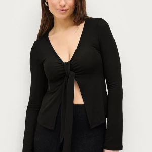 Svart långärmad topp med knyt - Säljer en svart långärmad topp med djup v-ringning och knyt framtill. Toppen har en figurnära passform och är tillverkad i ett mjukt, stretchigt material. Perfekt att styla med både kjol och byxor för en trendig look.
