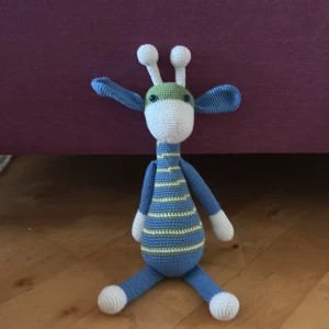 Virkad giraff i blått och grönt - Säljer en handvirkad giraff i mjukt garn. Giraffen har blå och gröna ränder på kroppen, blå ben och öron samt vita detaljer på ansikte, armar och fötter. Perfekt som present eller dekoration i barnrummet.