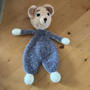 Stickad nallebjörn i grått och vitt - Söt stickad nallebjörn med mjuk grå kropp och vita tassar. Huvudet är beige med broderade svarta ögon och nos. Perfekt som gosedjur eller dekoration i barnrummet.