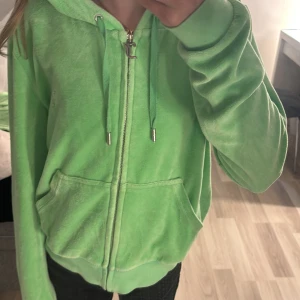 Grönt juciy set från Juicy Couture - Säljer en ljusgrönt juciy set  i mjuk velour från Juicy Couture. Jackan har dragkedja, huva med snören och två fickor framtill. Broderad JC-logga på bröstet. Perfekt för en avslappnad och trendig look.