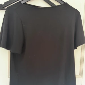 Svart topp från H&M - Enkel svart tröja  från H&M med korta ärmar och rund halsringning. Perfekt basplagg som är lätt att styla med accessoarer. Mjuk och bekväm, passar till många tillfällen.