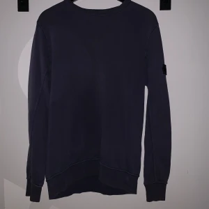 Mörkblå sweatshirt från Stone Island Junior - Säljer en mörkblå sweatshirt från Stone Island Junior. Tröjan har rund halsringning, långa ärmar och klassisk patch på ena ärmen. Perfekt för en stilren och avslappnad look. Storlek 170 Junior