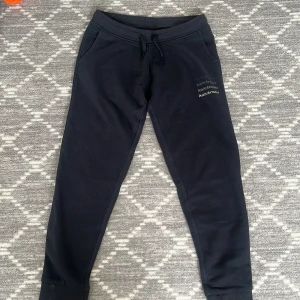 Mörkblåa mjukisbyxor från Peak Performance - Svarta mjukisbyxor från Peak Performance med dragsko i midjan och ribbade muddar vid bensluten. Byxorna har fickor på sidorna och diskret logga på låret. Perfekta för chill eller träning.