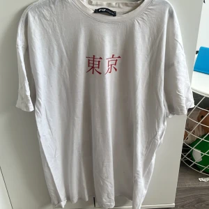 Vit t-shirt med Tokyo-tryck från FB Sister - Vit t-shirt från FB Sister med rött japanskt tecken på framsidan och stor grafisk print med koi-fiskar och texten 'TOKYO JAPAN' på baksidan. Klassisk passform och rund halsringning. Perfekt för dig som gillar streetstyle och unika prints. Oversized 