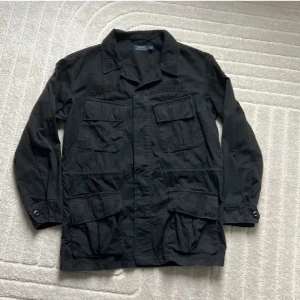 Svart fieldjacket/overshirt från Polo Ralph Lauren - Säljer en fet fieldjacket overshirt från Polo Ralph Lauren. Säljer p.ga jag har köpt en ny och denna inte kommer till användning längre. Den är i bra skick finns inga hål eller märkvärdiga slitningar. Det är bara att fråga ifall ni har några funderingar!