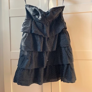 prickig klänning med volanger - Snygg svart axelbandslös klänning med vita prickar och flera lager av volanger. 