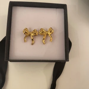 Guldörhängen med rosett - Eleganta örhängen i form av rosetter i guld. Perfekta för att ge en stilfull touch till din outfit. Kommer i en fin presentask. I stainless steel, aldrig använda 
