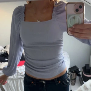 Ljuslila topp med långa ärmar - Säljer en söt ljuslila topp med långa ärmar och fyrkantig halsringning. Toppen har en smickrande tight passform och är perfekt för både vardag och fest. Den har en lätt rynkad detalj vid axlarna som ger en extra touch.