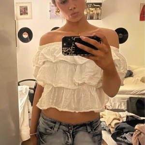 Vit offshoulder blus med volanger - Säljer en söt vit offshoulder blus med flera lager av volanger. Perfekt för en somrig look. Blusen är luftig och har en romantisk stil. Passar bra till jeans eller kjol för en avslappnad stil.
