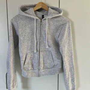 Ljusgrå zip hoodie med dragkedja - Säljer en ljusgrå hoodie från H&M med dragkedja framtill och huva med snören. Tröjan har två fickor fram och är croppad i modellen. Perfekt för en avslappnad stil. Aldrig används, pris kan diskuteras🤗