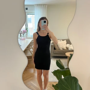 Svart ribbad klänning - Snygg svart ribbad klänning med smala axelband och en figurnära passform. Perfekt för en stilren look. Klänningen är ärmlös och har en klassisk design som passar till många tillfällen.