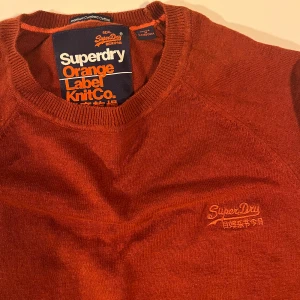 Rostfärgad tröja från Superdry - Säljer en snygg rostfärgad tröja från Superdry. Tröjan har en broderad logga på bröstet och är tillverkad i ett mjukt material. S/Xs 