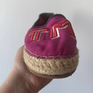 Rosa espadrillos från Tommy Hilfiger - Snygga rosa espadrillos från Tommy Hilfiger med broderad logga i rött och vitt. Skorna har en klassisk espadrillesula i naturmaterial och en bekväm passform. Perfekta för sommarens äventyr!