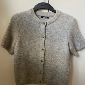 Grå kortärmad kofta från Gina Tricot - Supermjuk och stilren grå kofta från Gina Tricot med korta ärmar och pärlknappar framtill. Knappt använd och i nyskick, perfekt till våren!!