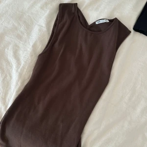 Brun ärmlös topp från Zara - Säljer en brun ärmlös topp från Zara i ribbad bomull. Toppen har en snygg, figurnära passform och coola sömdetaljer på ryggen som ger en modern look. Perfekt att styla med jeans eller kjol för en trendig vibe.