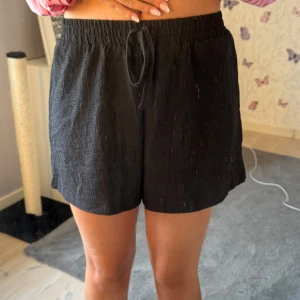 Svarta shorts med snörning - Svarta shorts i ett lätt linne likt material, med elastisk midja och snörning framtill. Använda max två ggr🩷