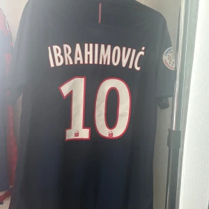 PSG Zlatan Ibrahimovic #10 Nike fotbollströja  - Paris Saint-Germain matchtröja med Ibrahimovic och nummer 10 på ryggen. Mörkblå med röda och vita detaljer, Fly Emirates tryck på bröstet och PSG-märke. Kortärmad, Dri-Fit material, Champion 2015 badge på ärmen. Snyggt randigt mönster framtill.