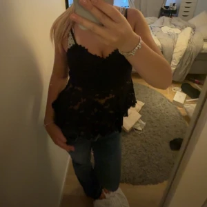Svart spetsig linnetopp med volang - Supersnygg svart linnetopp med spetsdetaljer och volang nertill. Toppen är ärmlös med smala axelband och har en feminin, lite romantisk look. Perfekt att styla med jeans eller kjol för en trendig outfit. Verkligen jättefin men kommer ej till användning! Köpte på en marknad så märke okänt! Storlek står inte men passar mig som brukar bära S!