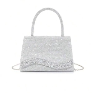 Glittrig silver handväska med kedja - Superfin handväska i silver med glittrande yta och en vågig detalj av paljetter på framsidan. Väskan har ett stadigt handtag och en tunn kedja som axelrem. Perfekt storlek för mobilen och det viktigaste. Snygg och unik design som verkligen sticker ut.
