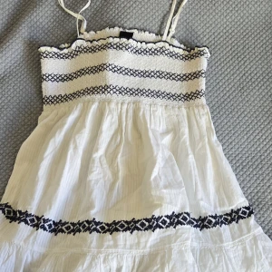 Vit topp - Supersöt vit lång topp från Vila med smala axelband och broderade svarta mönster. Toppen har smock upptill, volanger och ett flowigt tyg i bomull. Passar stl s-L! Perfekt för varma dagar och har en boho-vibe med sina detaljer och mönster! Snygga topp! Passar till jeans och att croppa den lite! Skriv om du är intresserad eller har några frågor! Pris kan diskuteras!