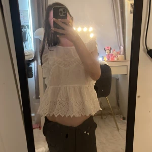 Vit blus med volang och broderi - Supersöt vit blus med volangärmar och broderade detaljer. Toppen har en luftig passform, rund hals och vackert hålbroderi längs nederkanten. Perfekt för en romantisk look och passar till både jeans och kjol. Väldigt liten i storlek!!!